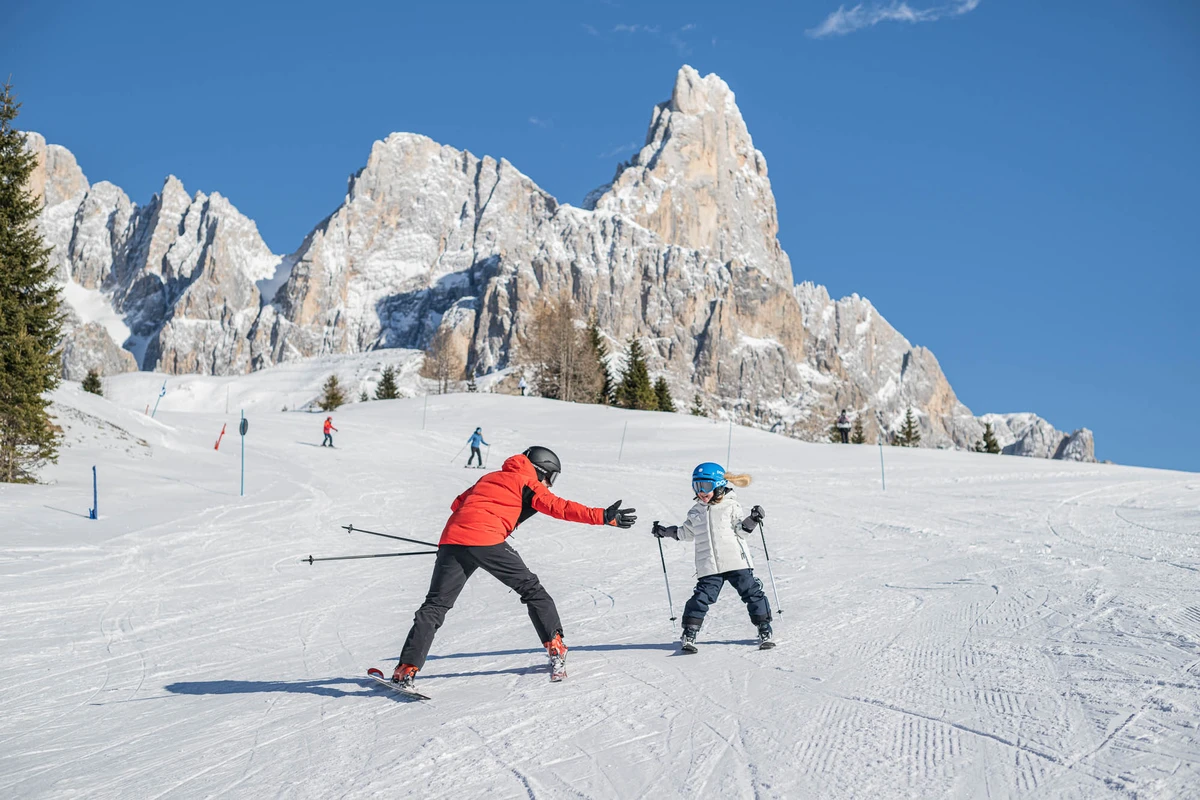 A parent and child high-five on the piste in front of a jagged Dolomite mountain rock massif