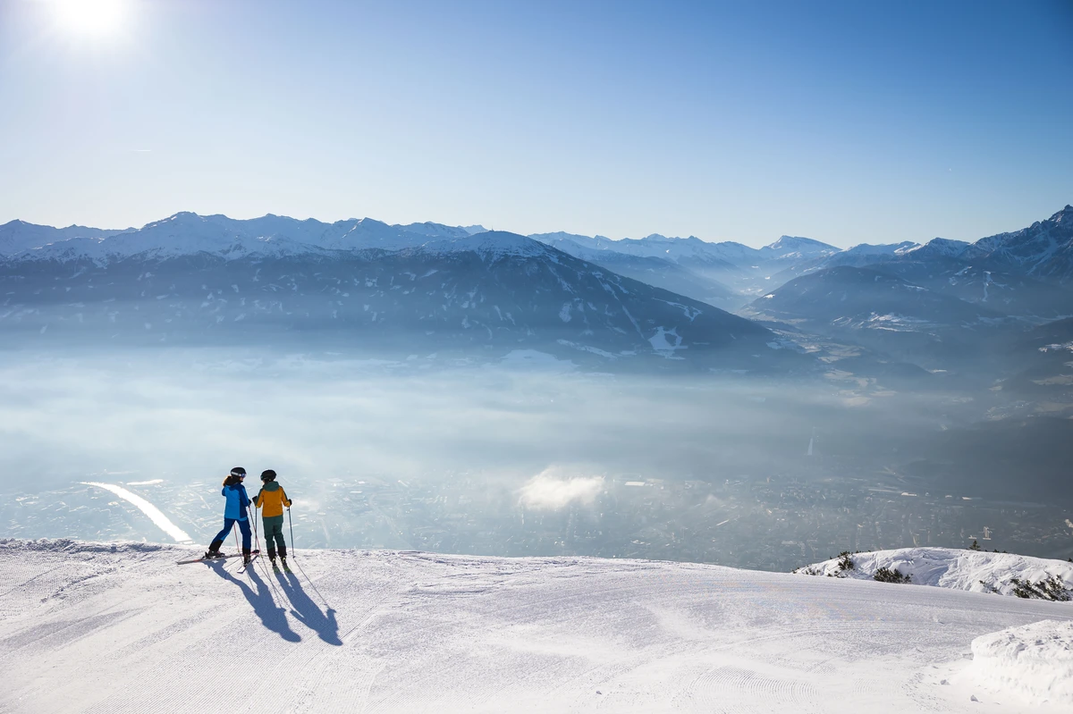 two skiers stand atop a hill looking out over a valley view